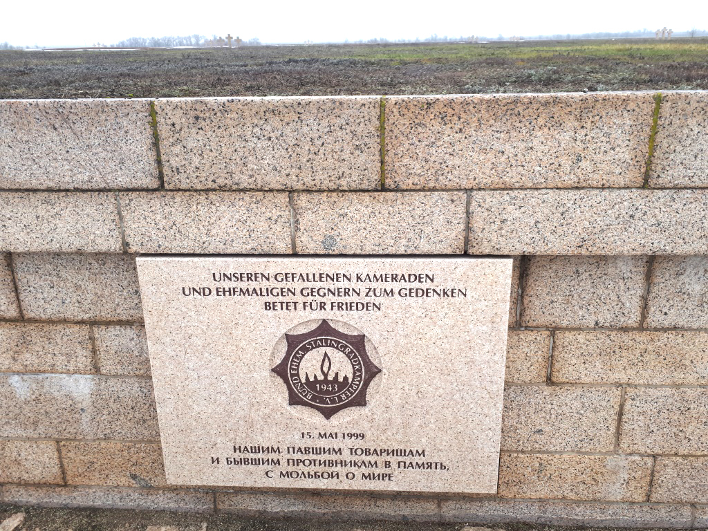 A memorial plate on the German side of the cemetery with the inscription in German and Russian: "To Our Fallen Comrades and Former Foes in Memory of the Prayer for Peace"